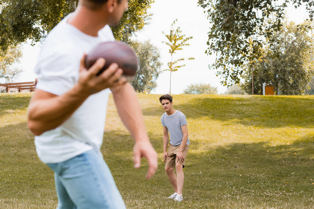 избирательный фокус подростка, смотрящего на отца, держащего регби-мяч  - Фото, изображение