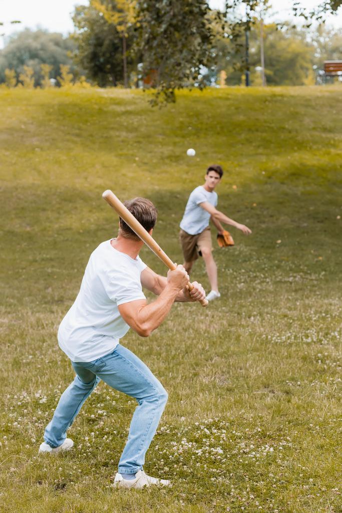 vista posterior del padre sosteniendo el bate de softbol mientras juega béisbol con un adolescente  - Foto, imagen