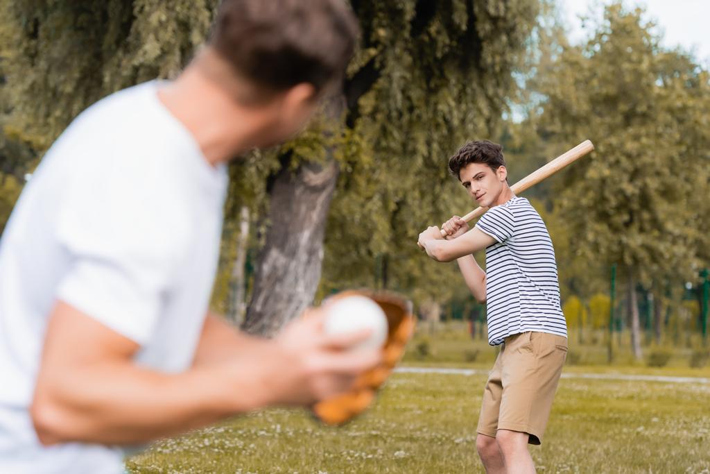 selektivní zaměření teenager chlapec drží softball bat a hraje baseball s mužem v parku - Fotografie, Obrázek