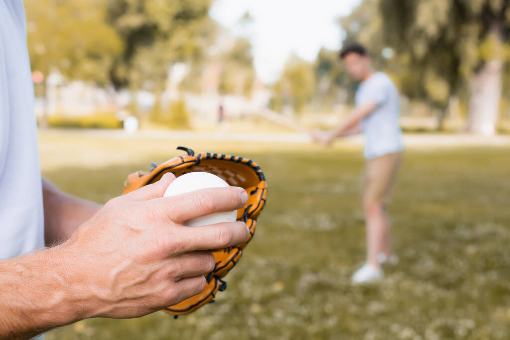 częściowy widok człowieka w skórzanej rękawicy gospodarstwa piłkę w pobliżu nastolatek syn w parku  - Zdjęcie, obraz