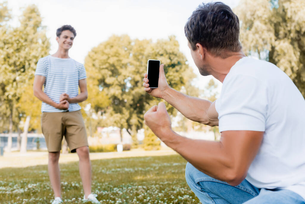 スマートフォンを持っていて公園で10代の息子の写真を撮るという選択的な焦点は  - 写真・画像