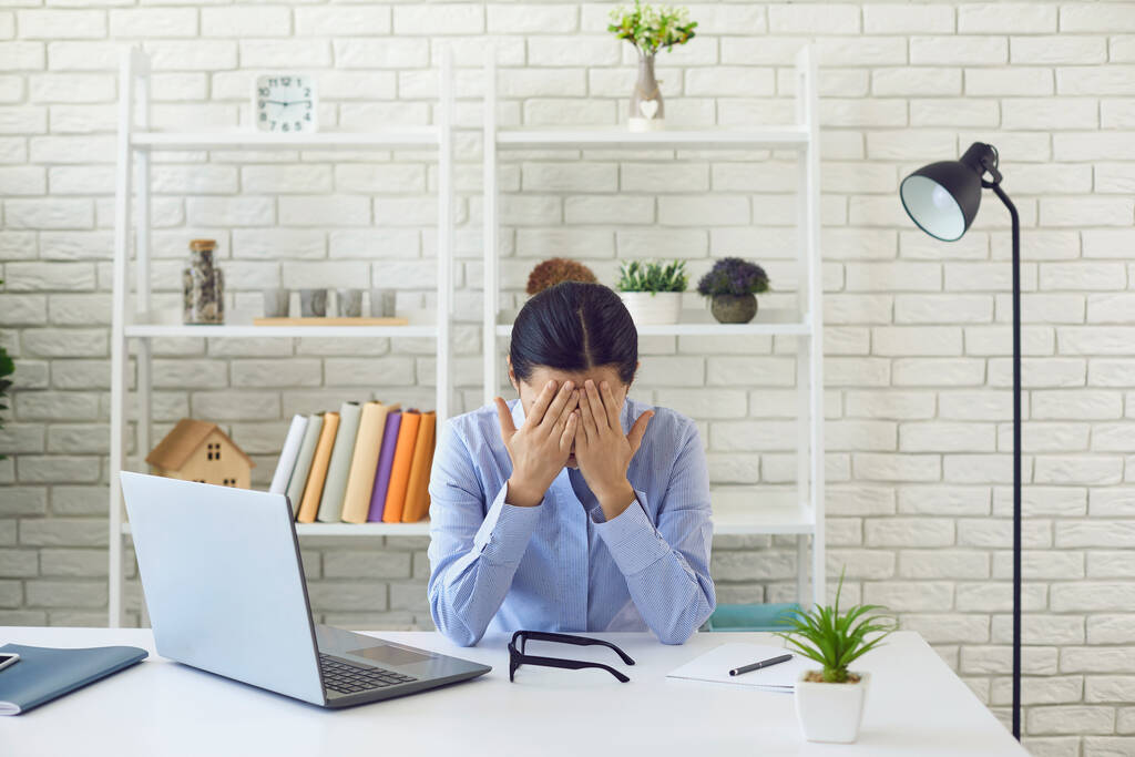 Vyčerpaná mladá žena pracující přesčas v kanceláři. Žena zaměstnankyně trpí pracovním stresem na svém stole - Fotografie, Obrázek