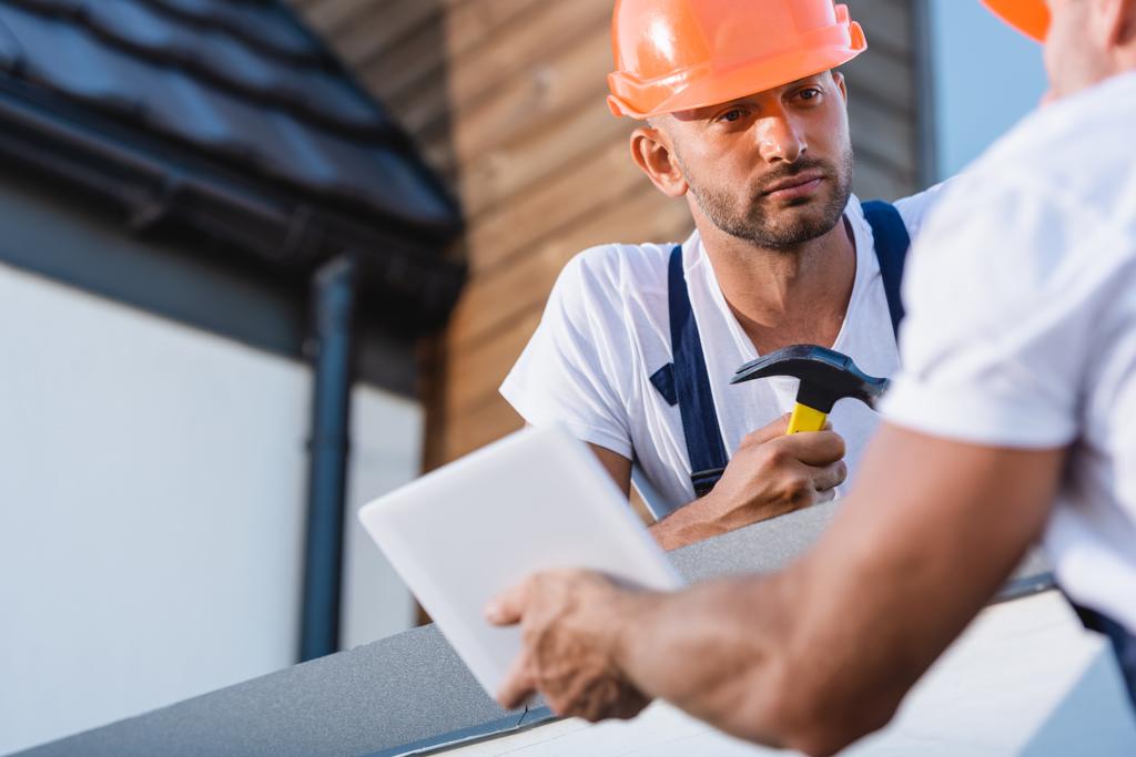 Enfoque selectivo del constructor con martillo mirando a colega con tableta digital en el techo del edificio  - Foto, Imagen