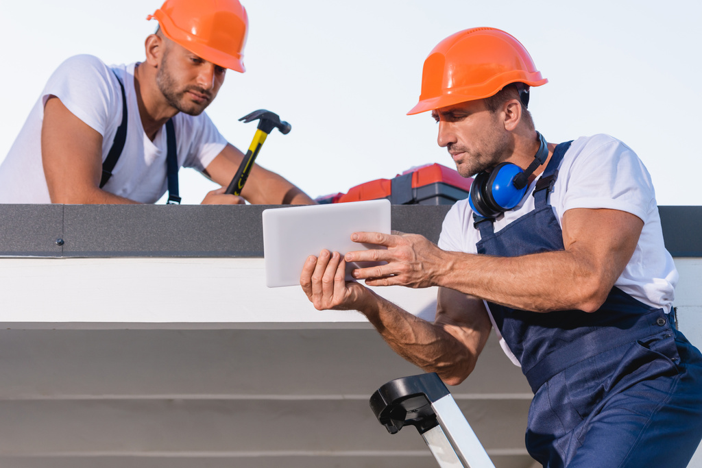 Reparaturtrupps in Overalls und Helmen mit digitalem Tablet auf Hausdach  - Foto, Bild