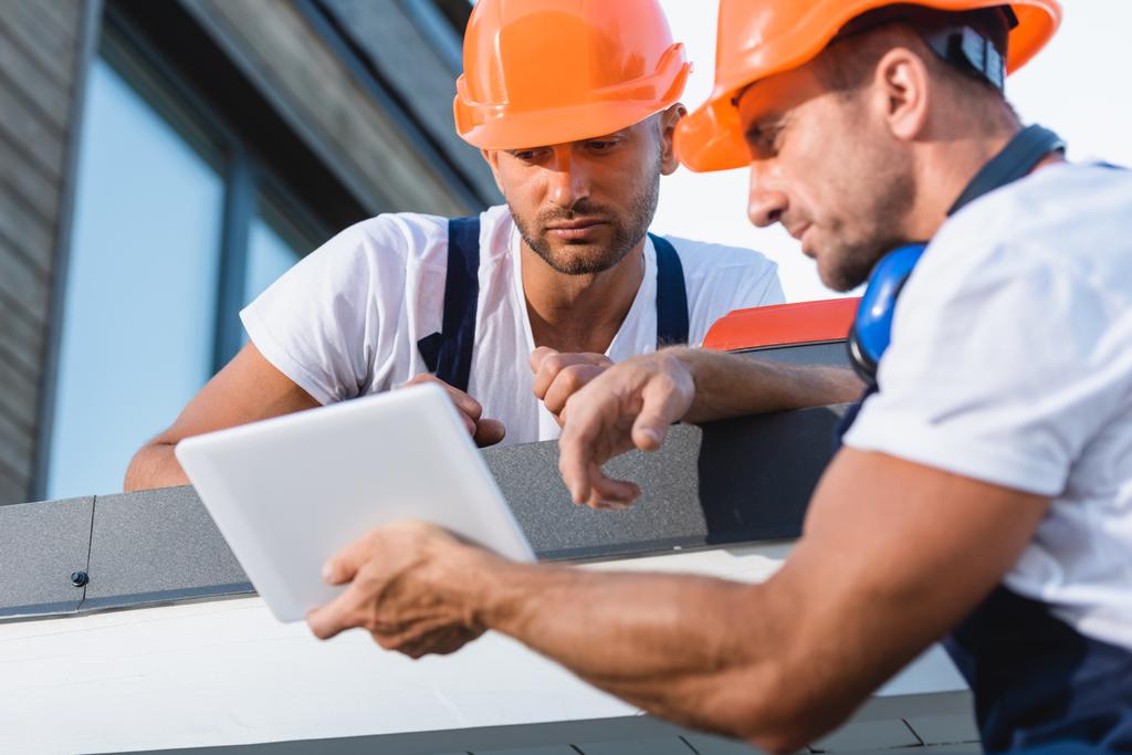 Foco seletivo de trabalhadores manuais olhando para tablet digital no telhado da casa  - Foto, Imagem