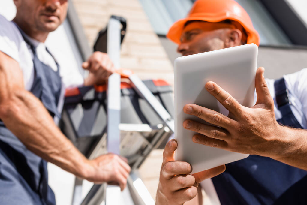 Selektiver Fokus der Heimwerker mit digitalem Tablet beim Arbeiten mit Leiter in der Nähe von Gebäuden  - Foto, Bild