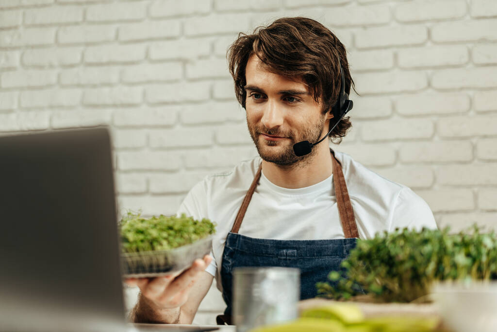 Handsome bearded man sells plant sprouts and seedlings online using laptop - Photo, Image