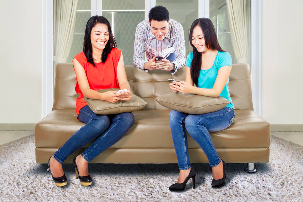 Gruppo di giovani che utilizzano il proprio smartphone per navigare in internet godendo del tempo libero a casa - Foto, immagini