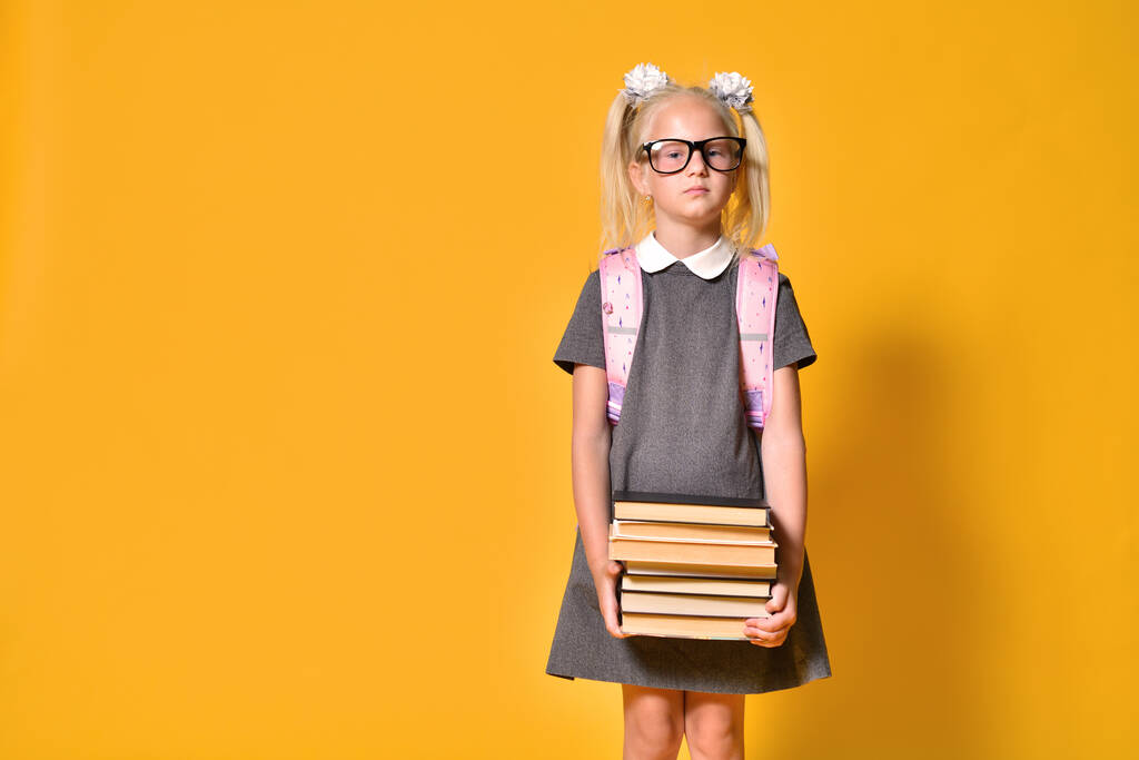 Dziewczyna uczennica szkoły podstawowej stoi niezadowolony z stosu ciężkich książek - Zdjęcie, obraz