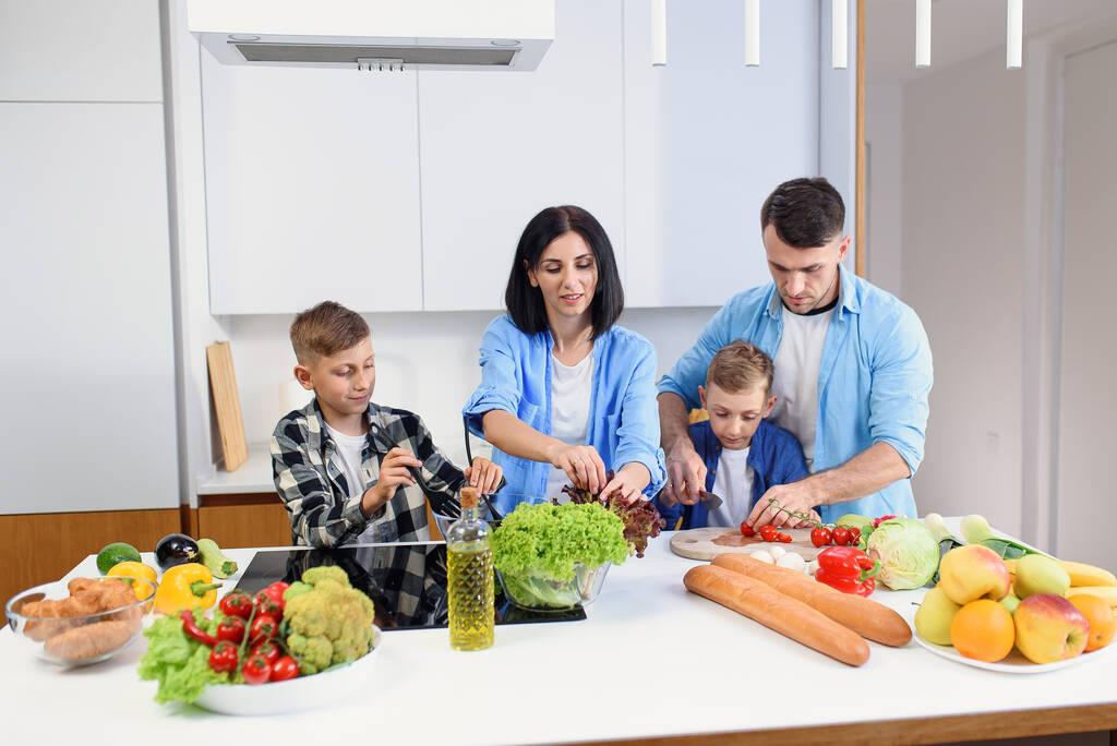 Heureuse famille caucasienne avec deux fils préparant un petit déjeuner végétarien sain avec et légumes sur une cuisine confortable. - Photo, image