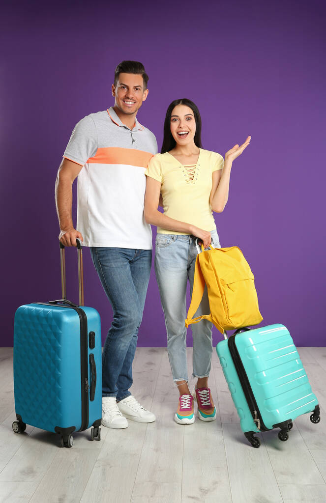 Boldog pár bőröndökkel a nyári kiránduláshoz a lila fal mellett. Nyaralás utazás - Fotó, kép