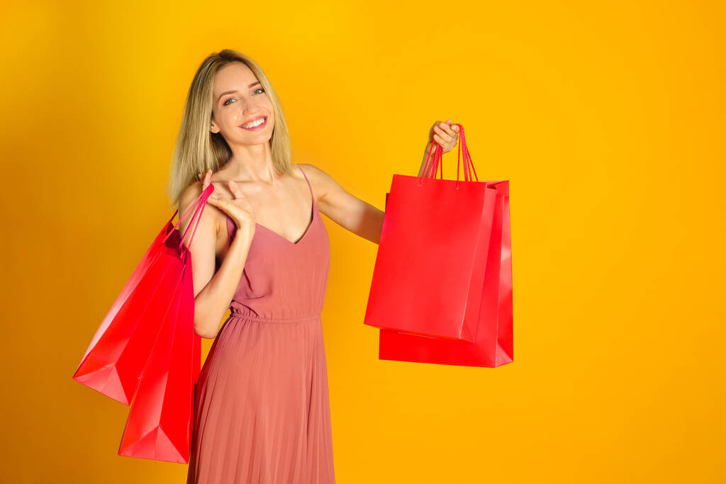 Glückliche junge Frau mit Einkaufstaschen auf gelbem Hintergrund. Black Friday Sale - Foto, Bild