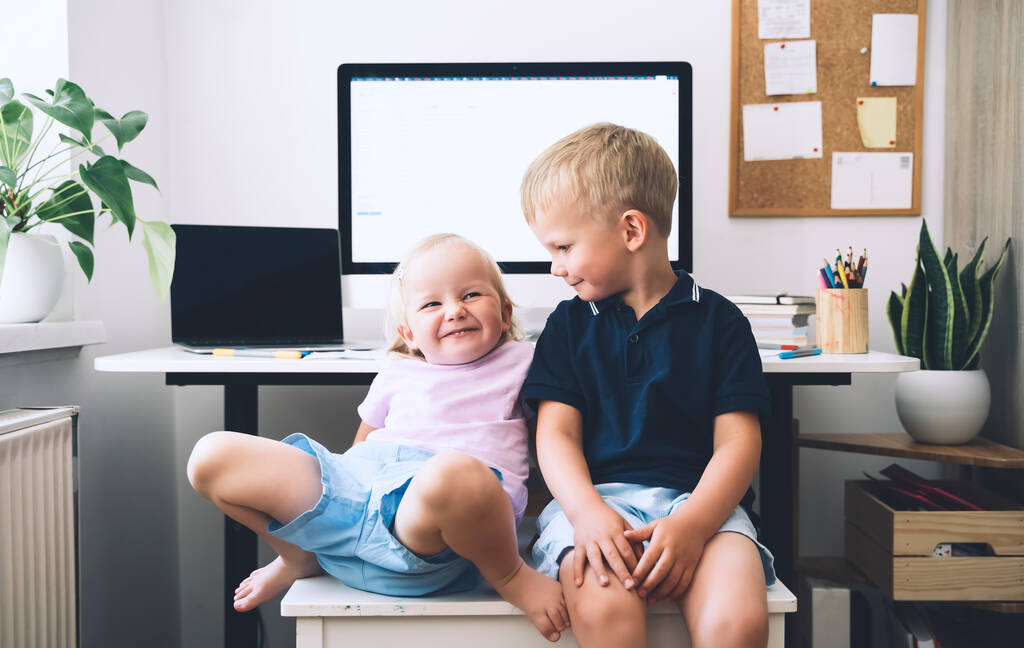 Portrait of preschool boy and girl on background of computer with blank white screen in home interior. Kids and computer technologies. Children online learning, development or entertainment. - Photo, Image