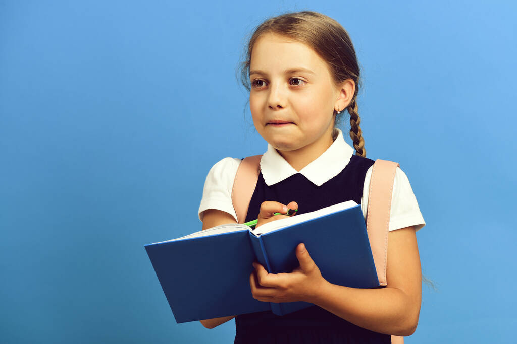 Dziewczyna pisze w wielkim niebieskim zeszycie. Uczeń w szkolnym mundurze - Zdjęcie, obraz