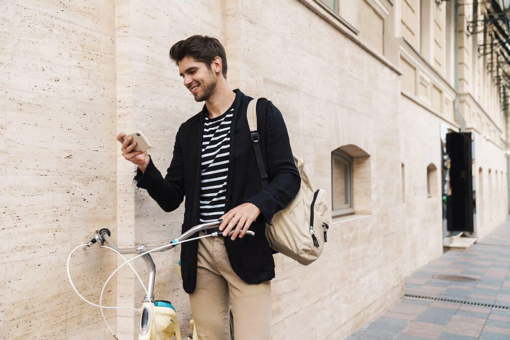 Wizerunek młodego uśmiechniętego biznesmena na zewnątrz, korzystającego z telefonu komórkowego na rowerze - Zdjęcie, obraz