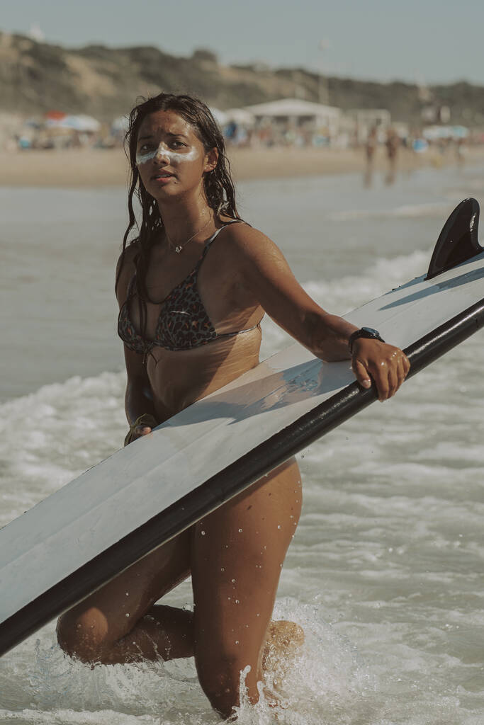 Eine vertikale Aufnahme einer schönen jungen Frau mit einem Surfbrett am Strand - Foto, Bild