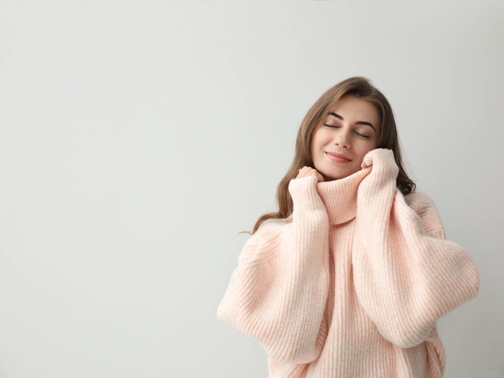 Piękna młoda kobieta w ciepłym różowym swetrze na jasnym tle. Miejsce na tekst - Zdjęcie, obraz