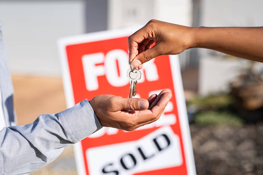 Saleswoman giving home keys to new property owner. Close up of real estate agent hand giving house keys to indian man. Agent giving apartment key to new owner after putting the word sold on for sale sign outside the house. - Photo, Image