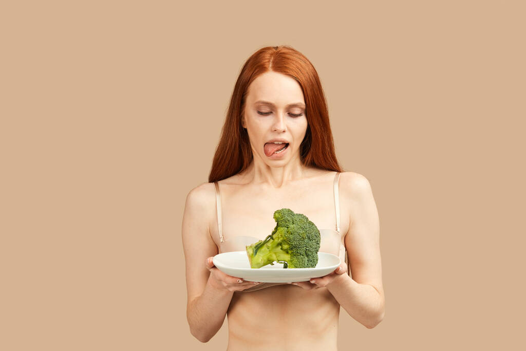 Femme maigre en sous-vêtements tenant brocoli, lécher, veut le manger beaucoup - Photo, image