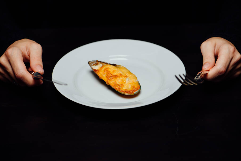 pečená slávka ve skořápce se sýrem na bílém talíři s nožem a vidličkou na černém pozadí - Fotografie, Obrázek