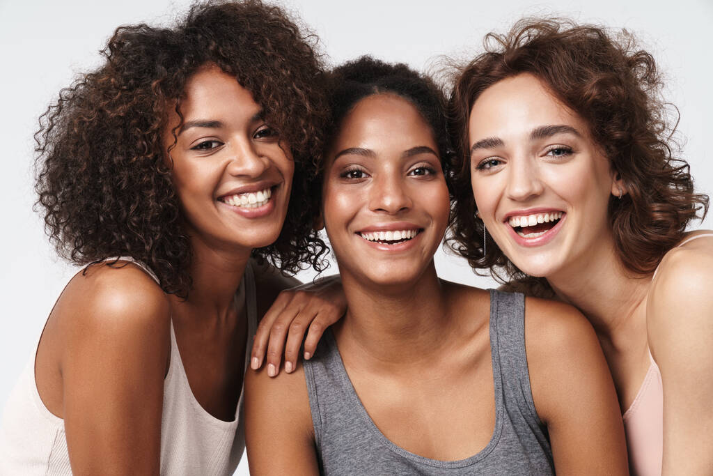 Portret trzech młodych wielorasowych kobiet stojących razem i uśmiechających się do kamery odizolowanych na białym tle - Zdjęcie, obraz