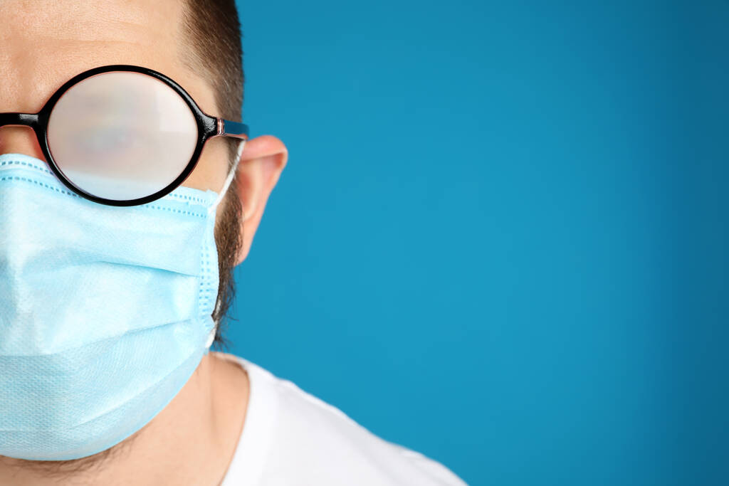 Hombre con gafas de niebla causada por el uso de máscara desechable sobre fondo azul, espacio para el texto. Medida de protección durante la pandemia del coronavirus - Foto, imagen