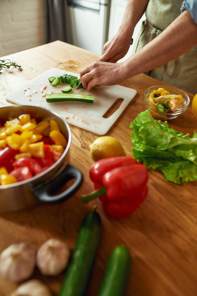 Sebze doğrayan ve sağlıklı yemek hazırlarken tencereye koyan adamın ellerini kapat. Mutfakta çorba. - Fotoğraf, Görsel