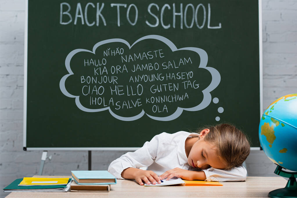 colegiala agotada durmiendo en el escritorio cerca de globo y pizarra con letras de regreso a la escuela y saludo - Foto, Imagen