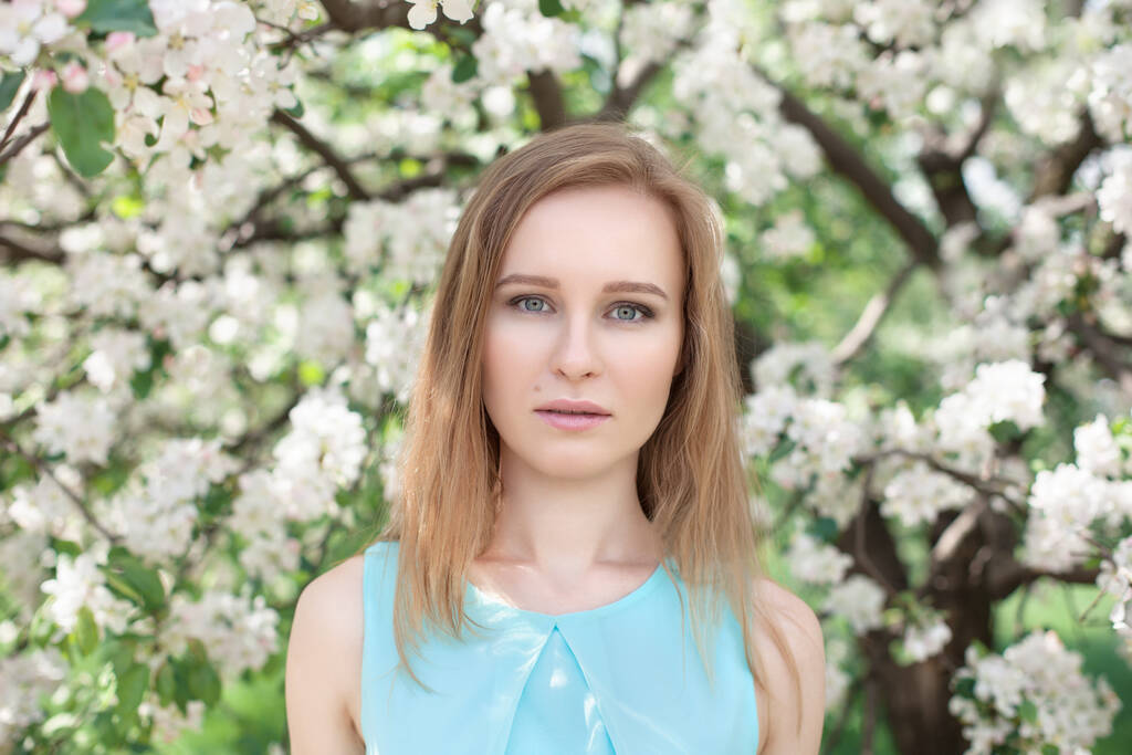 portrét mladé blondýny v modrých šatech. stromy v květinách. - Fotografie, Obrázek