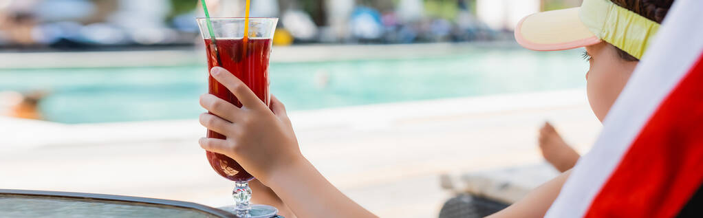horizontaal beeld van meisje in zonneklep met cocktailglas terwijl ze in de ligstoel rust - Foto, afbeelding