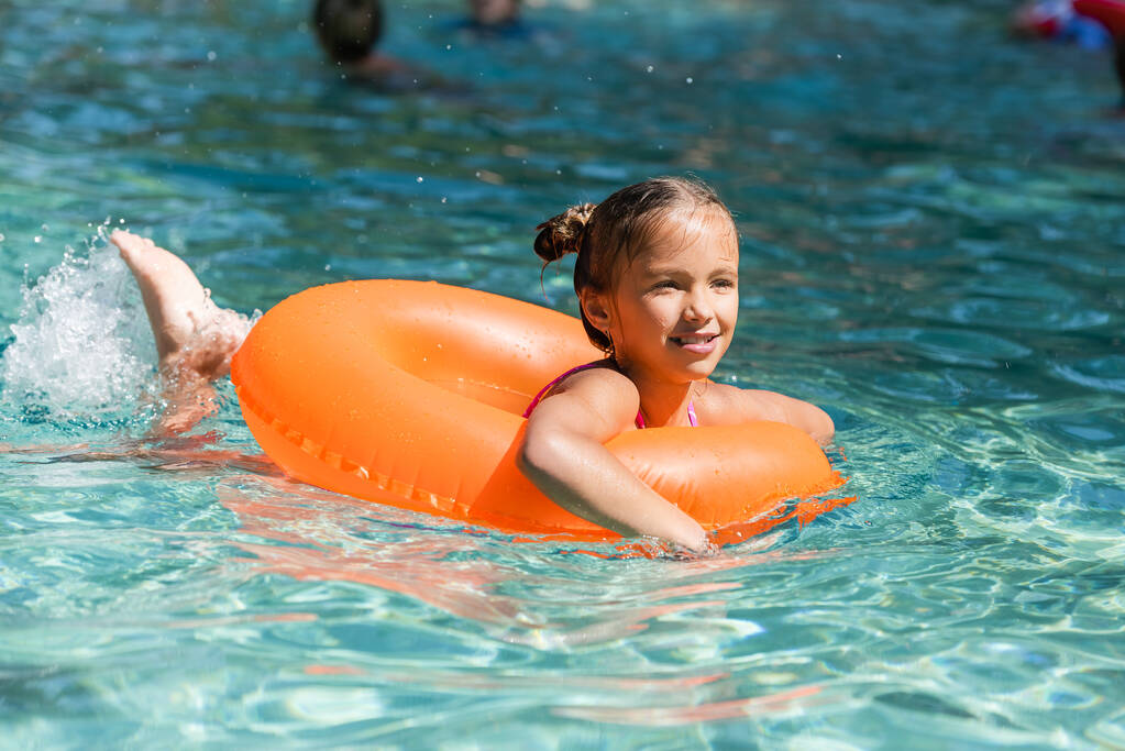 criança flutuando na piscina no anel de natação ao fazer respingos de água com pernas - Foto, Imagem