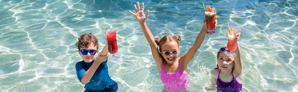 colheita panorâmica de meninas e menino de pé na piscina e segurando coquetéis refrescantes em mãos levantadas - Foto, Imagem