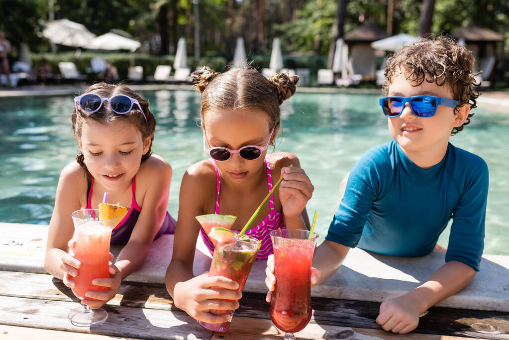 дівчина в купальнику тримає соломинку біля друзів зі свіжими фруктовими коктейлями на березі басейну
 - Фото, зображення