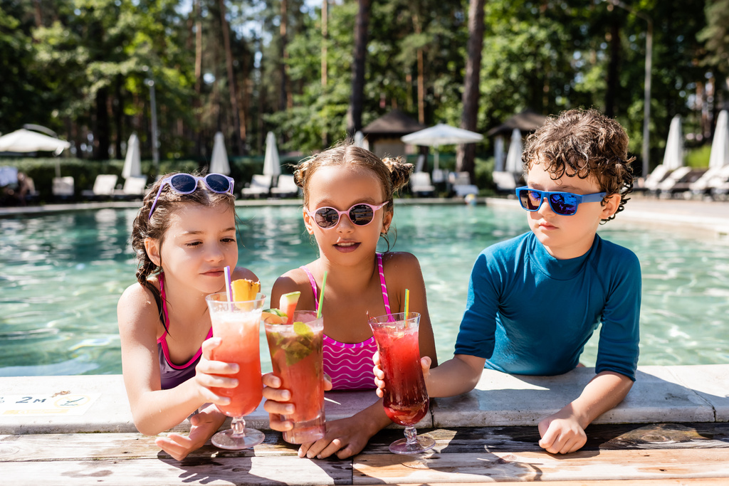 amis en maillots de bain cliquetis avec des cocktails de fruits frais près de la piscine - Photo, image