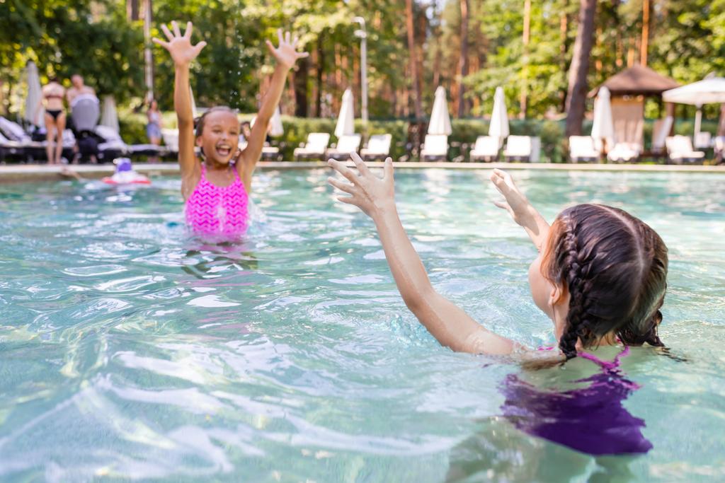 興奮した女の子の選択的な焦点を手で空気中で友人とプールで楽しみを持っている - 写真・画像