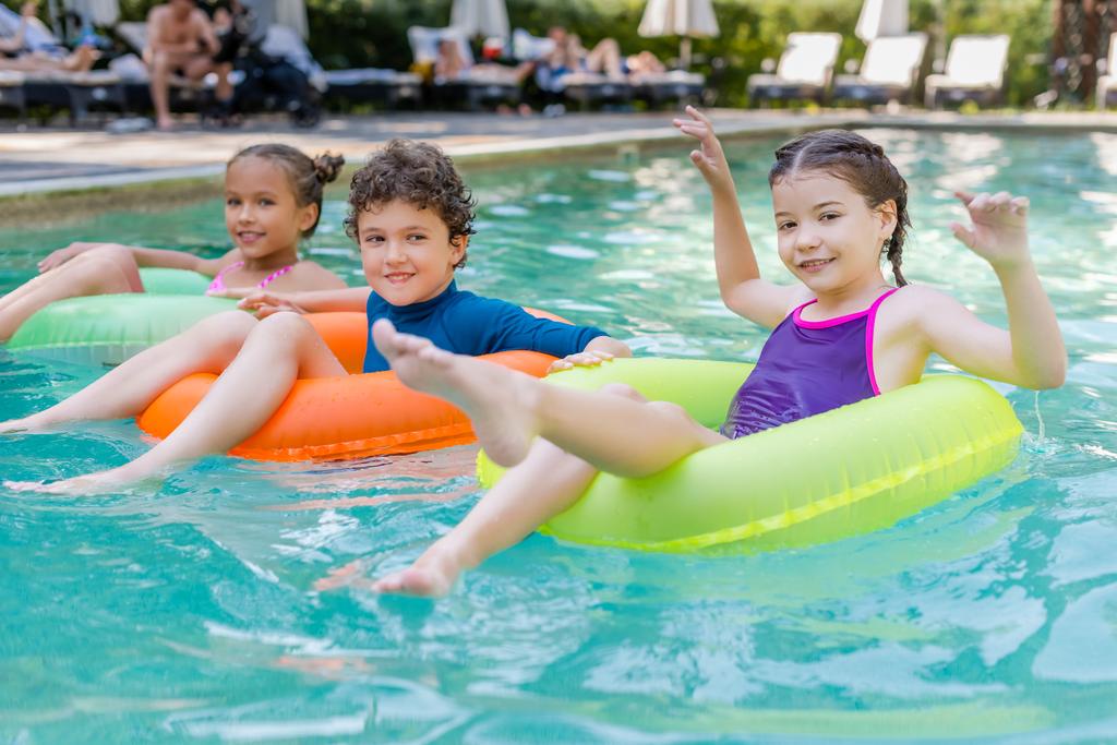 радісні друзі дивляться на камеру, плаваючи в басейні на різнокольорових кільцях для плавання
 - Фото, зображення