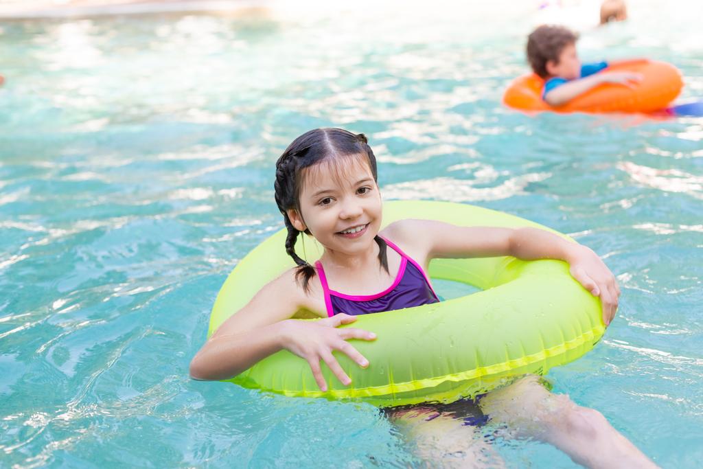 freudiges Mädchen blickt in die Kamera, während es im Pool auf dem Schwimmring schwimmt - Foto, Bild