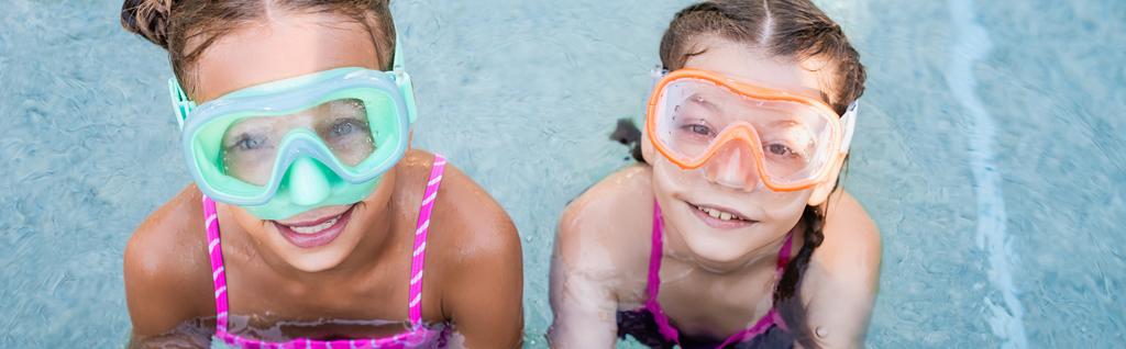 プールサイド横の作物の近くのカメラを見て泳ぐマスクの2人の女の子のオーバーヘッドビュー - 写真・画像