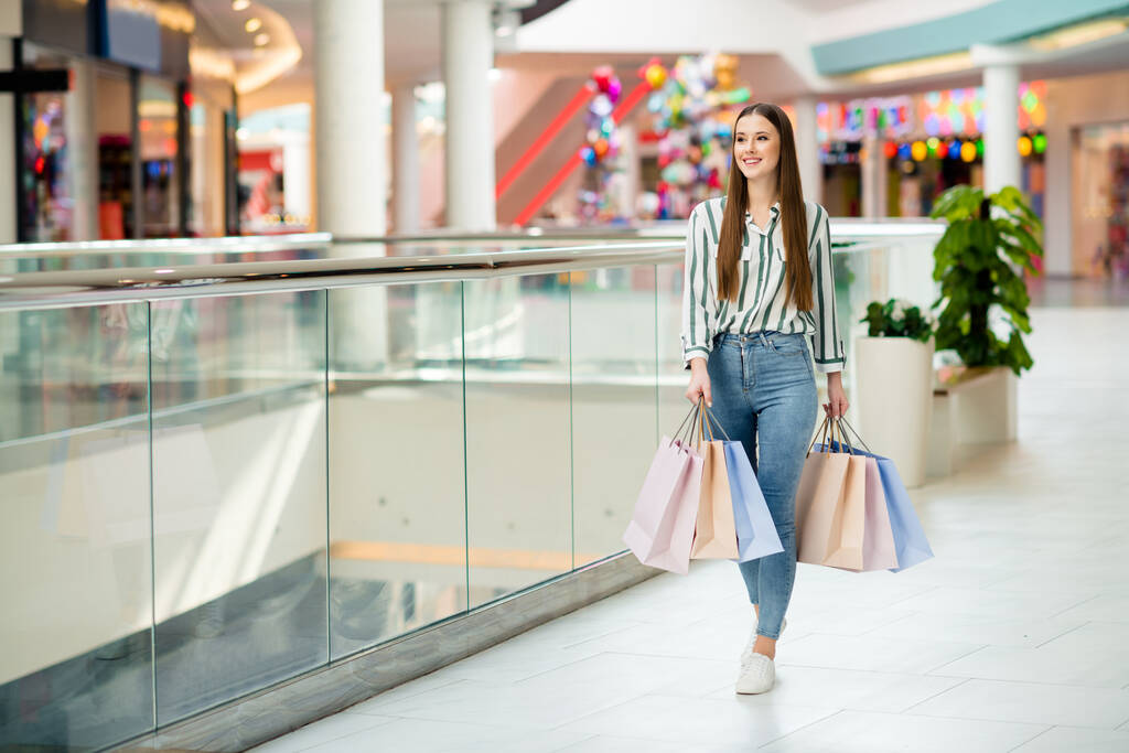 Фотографія веселої красивої дівчини, яка насолоджується вільним часом, купує багато сумки, що йдуть по поверху торгового центру, збуджених відвідати наступний магазин одягати повсякденні джинсові сорочки взуття в приміщенні
 - Фото, зображення