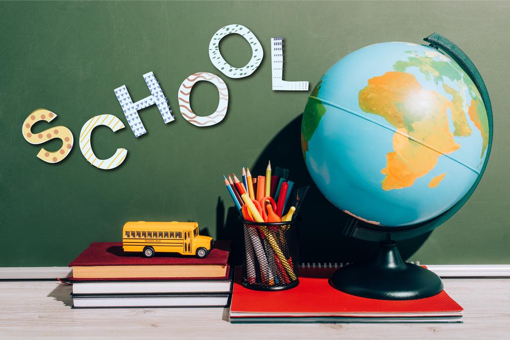 σφαίρα και κάτοχος στυλό για σημειωματάριο κοντά παιχνίδι σχολικό λεωφορείο για βιβλία κοντά στο πράσινο chalkboard με γράμματα σχολείο  - Φωτογραφία, εικόνα
