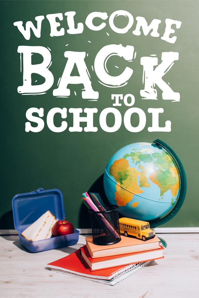 globo vicino giocattolo scuolabus e portapenne su libri vicino al cestino del pranzo e lavagna verde con iscrizione a scuola  - Foto, immagini