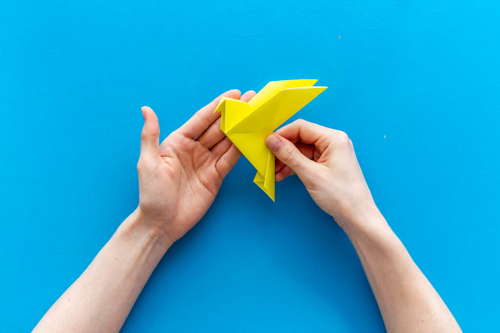 Origami pájaro en manos femeninas. Cuidado concepto de paz. Vista superior - Foto, imagen
