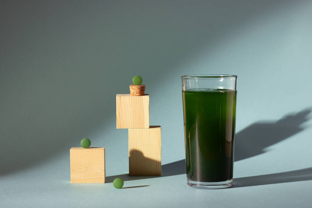 Spirulina ή chlorella δισκία και γυαλί με chlorella ποτό σε μπλε φόντο. Φως με σκιές. - Φωτογραφία, εικόνα