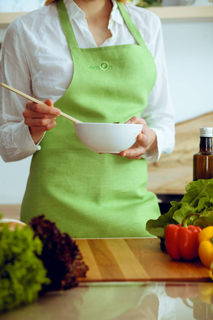 Άγνωστα ανθρώπινα χέρια μαγειρεύουν στην κουζίνα. Η γυναίκα είναι απασχολημένη με τη σαλάτα λαχανικών. Υγιεινό γεύμα και χορτοφαγική έννοια των τροφίμων - Φωτογραφία, εικόνα