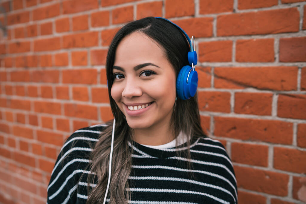 Retrato de una joven hermosa mujer escuchando música con auriculares azules en la calle. Al aire libre. - Foto, Imagen
