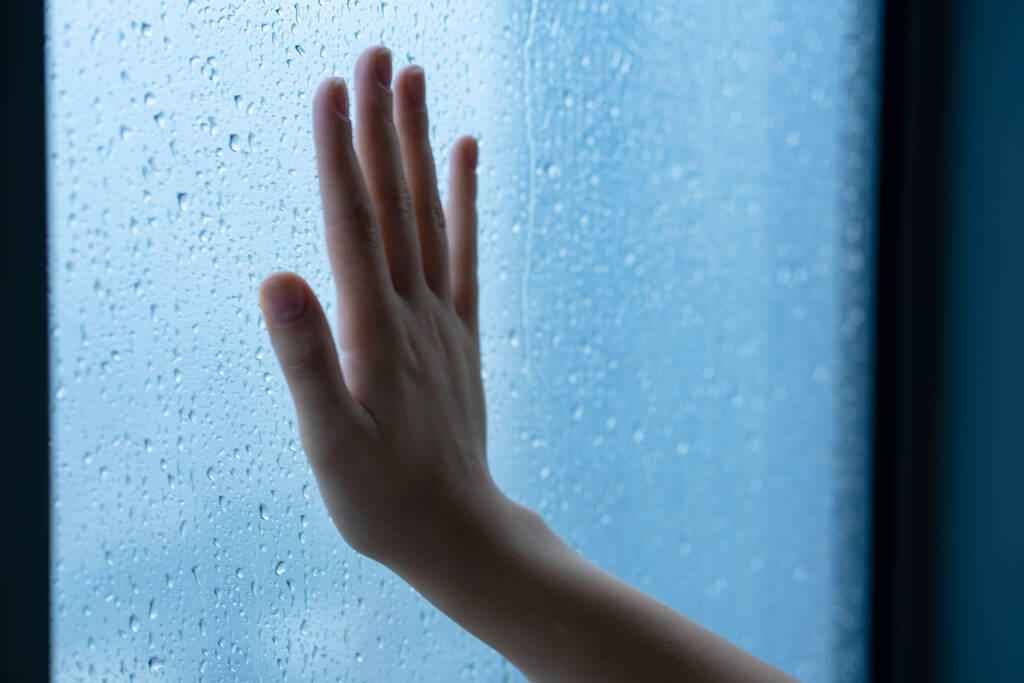 Kobieca ręka przy oknie podczas deszczu. Szkło w kroplach wody - Zdjęcie, obraz