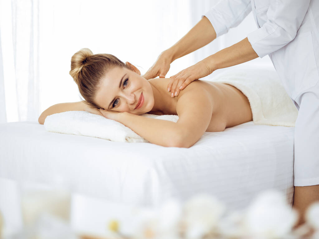 Jonge en blonde vrouw geniet van massage van rug in spa salon. Schoonheidsconcept - Foto, afbeelding