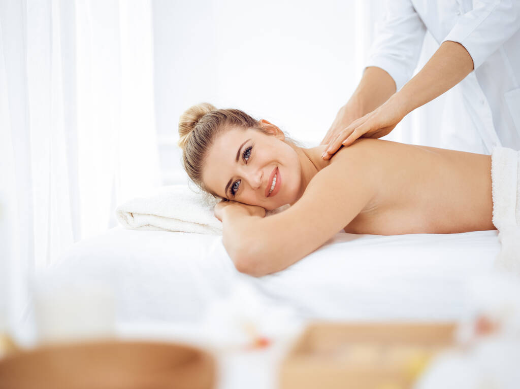 Mujer joven y rubia disfrutando del masaje de espalda en el salón de spa. Concepto de belleza - Foto, imagen