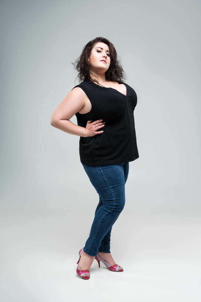 Além de modelo de moda tamanho em blusa preta e jeans azul, mulher gorda em fundo estúdio cinza, conceito corpo positivo - Foto, Imagem