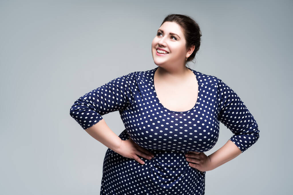 Счастливая модель plus size в синем платье из польки, толстая женщина на фоне студии, позитивное для тела понятие - Фото, изображение